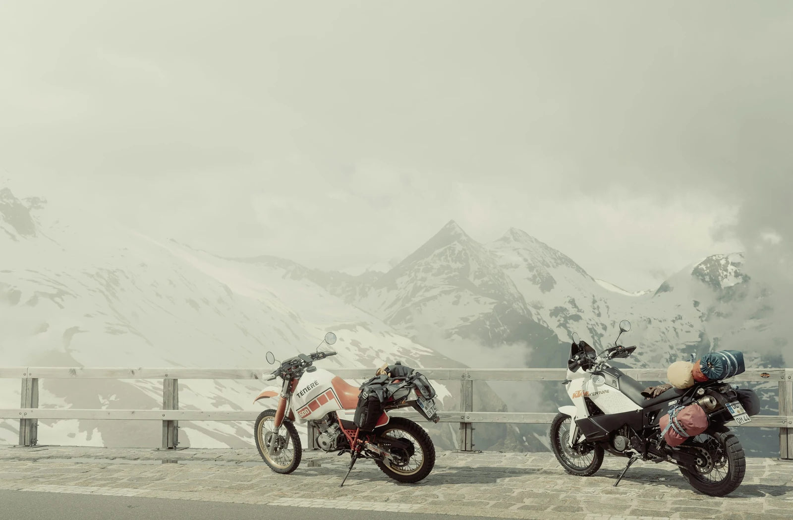 Two adventure motorcycles parked beneath snowy mountains